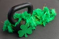 Black iron kettlebell with green feather boa on a black gym floor, holiday fitness, green shamrock