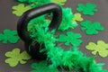 Black iron kettlebell with green feather boa on a black gym floor, holiday fitness, green shamrocks