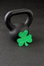 Black iron kettlebell and green glitter shamrock on a black gym floor, happy St. Patrickâs Day