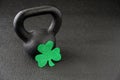 Black iron kettlebell and green glitter shamrock on a black gym floor, happy St. Patrickâs Day