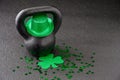 Black iron kettlebell, and green glitter shamrock and leprechaun hat, covered in green shamrock confetti on a black gym floor, hap