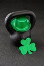 Black iron kettlebell and green glitter shamrock and leprechaun hat on a black gym floor, happy St. Patrickâs Day