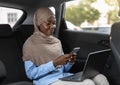 Black islamic businesswoman using smartphone and laptop, going to office by car Royalty Free Stock Photo