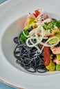 Black Italian seafood pasta with shrimps, cherry tomatoes and greens. Pasta with cuttlefish ink, cooked sea food macaroni Royalty Free Stock Photo