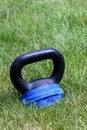 Black kettle bell with a blue face mask, on a green lawn, ready for an outdoor workout Royalty Free Stock Photo