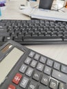 A black keyboard and a calculator rest side-by-side on a light desk.
