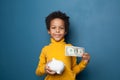 Black kid boy holding one us dollar and money box on blue background Royalty Free Stock Photo