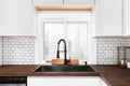 A black kitchen sink and faucet detail in a white kitchen with a butcher blocker countertop. Royalty Free Stock Photo