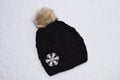 Black hat with furry ball and large snowflake on fresh snow. Royalty Free Stock Photo