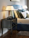 Black lacquered bedside table with table lamp and silver curly stand. The lampshade is square in shape