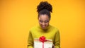 Black lady holding present, surprised with birthday gift, yellow background