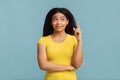 Black lady pointing finger up and looking upwards, having idea, found solution, standing on blue background Royalty Free Stock Photo