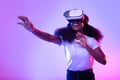 Black lady in VR glasses exploring cyberspace, touching imaginary screen, playing virtual reality game in neon light