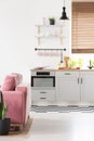 Black lamp above grey kitchenette in open space interior with pink sofa and window. Real photo
