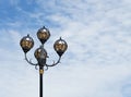 Black lamppost with three lamps and patterns on the background of blue sky with clouds Royalty Free Stock Photo