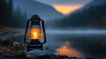 A black lantern with a yellow light sits on a rock by a lake, with a forest and mountains in the background. Royalty Free Stock Photo