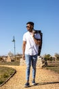 black latin man walking through a park in the street in the summer with a jacket over his shoulder. Vertical portrait Royalty Free Stock Photo