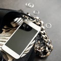 Black leather bag with chain, white phone, zebra print, silver thin rings on a black background. Top view. Copy space