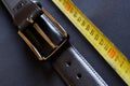 A black leather belt with holes and a metal buckle rests on a gray background next to a yellow tape measure. The concept of Royalty Free Stock Photo