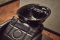 Black leather seat with wash basin in a barbershop interior with towels and shampoo on the side. Royalty Free Stock Photo