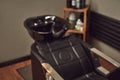 Black leather seat with wash basin in a barbershop interior with towels and shampoo on the side. Royalty Free Stock Photo