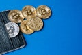 Black leather wallet on a blue background with several gold and silver coins of bitcoins falling out of their pockets.