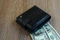 Black leather wallet, closed on the table. Under the purse are two banknotes of money