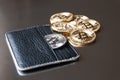 The black leather wallet on a dark background with several gold and silver coins of bitcoins falling out of their pockets.