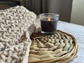 A black lighted candle in glass on a rattan stand and a plush beige plaid on the bed in the room. Royalty Free Stock Photo