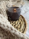 A black lighted candle in glass on a rattan stand and a plush beige plaid on the bed in the room. Royalty Free Stock Photo