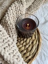 A black lighted candle in glass on a rattan stand and a plush beige plaid on the bed in the room. Royalty Free Stock Photo
