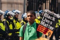 Black Lives Matter protest during lockdown coronavirus pandemic. Young man with BLM banner posing in front of Police officers