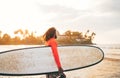 Black long-haired teen boy with a waxed surfboard ready for surfing with sunset backlight. He walking into Indian ocean waves. Royalty Free Stock Photo