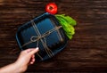 Black Lunch box tied with flagella. Food on dark brown wooden surface. Closed Box for food, tomato, cucumber and lettuce