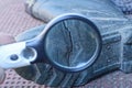 A black magnifier in the hand enlarges the crack on the sole of the green rubber boot