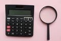 Close up black magnifying glass and calculator on pink pastel background.Business and finanse concept