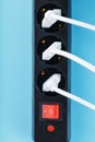 A black mains filter with electrical outlets inserted into it with white plugs of electrical appliances on a blue Royalty Free Stock Photo