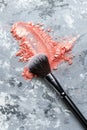 A black makeup brush with its bristles coated in orange powder