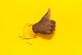 Black male gesturing thumb up, showing approval sign through hole in ripped yellow paper background, closeup