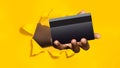 Black male hand holding bank credit card in torn hole of yellow background, panorama, closeup