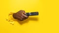 Black male hand holding remote control through the torn yellow paper background, pointing it aside at free space Royalty Free Stock Photo