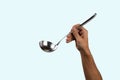 Black male hand holding a silver kitchen ladle isolated o cyan background Royalty Free Stock Photo