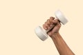 Black male hand holding a white dumbell isolated, light beige background