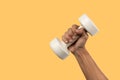 Black male hand holding a white dumbell isolated, yellow background.