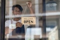 Black male shopkeeper wearing apron with open sign A waitress stands at the entrance to the cafe and food.