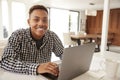 African American male teenager using a laptop computer at home smiling to camera, close up