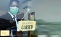 A black male waiter wearing an anti-virus mask holds a sign that says the store is closed