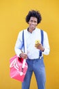 Black man with afro hairstyle carrying a sports bag and smartphone in yellow background. Royalty Free Stock Photo