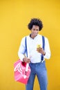 Black man with afro hairstyle carrying a sports bag and smartphone in yellow background. Royalty Free Stock Photo