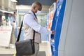 Black man buying a ticket to travel on public transport. He is wearing a medical mask